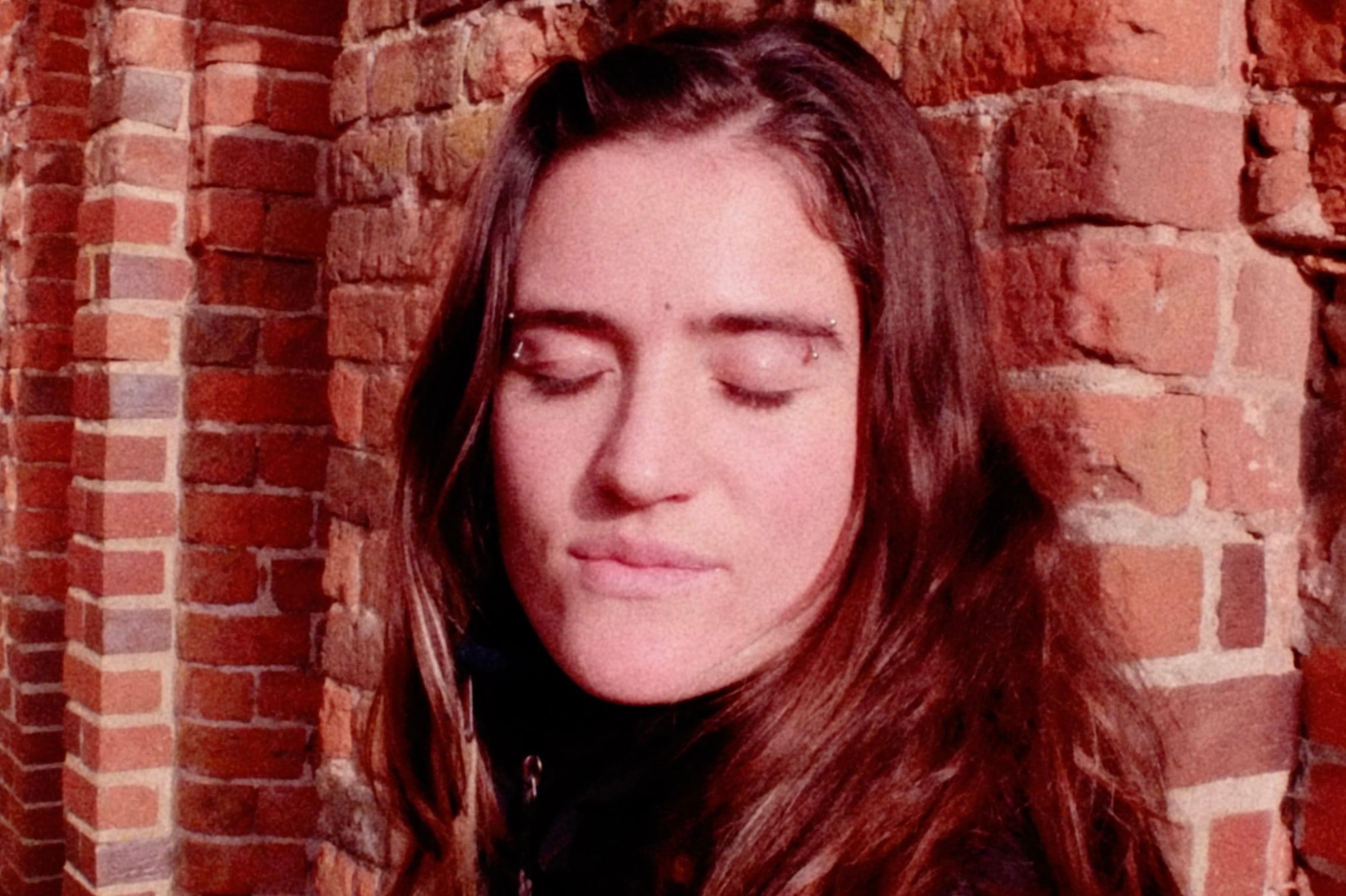 Woman with closed eyes against a red brick wall