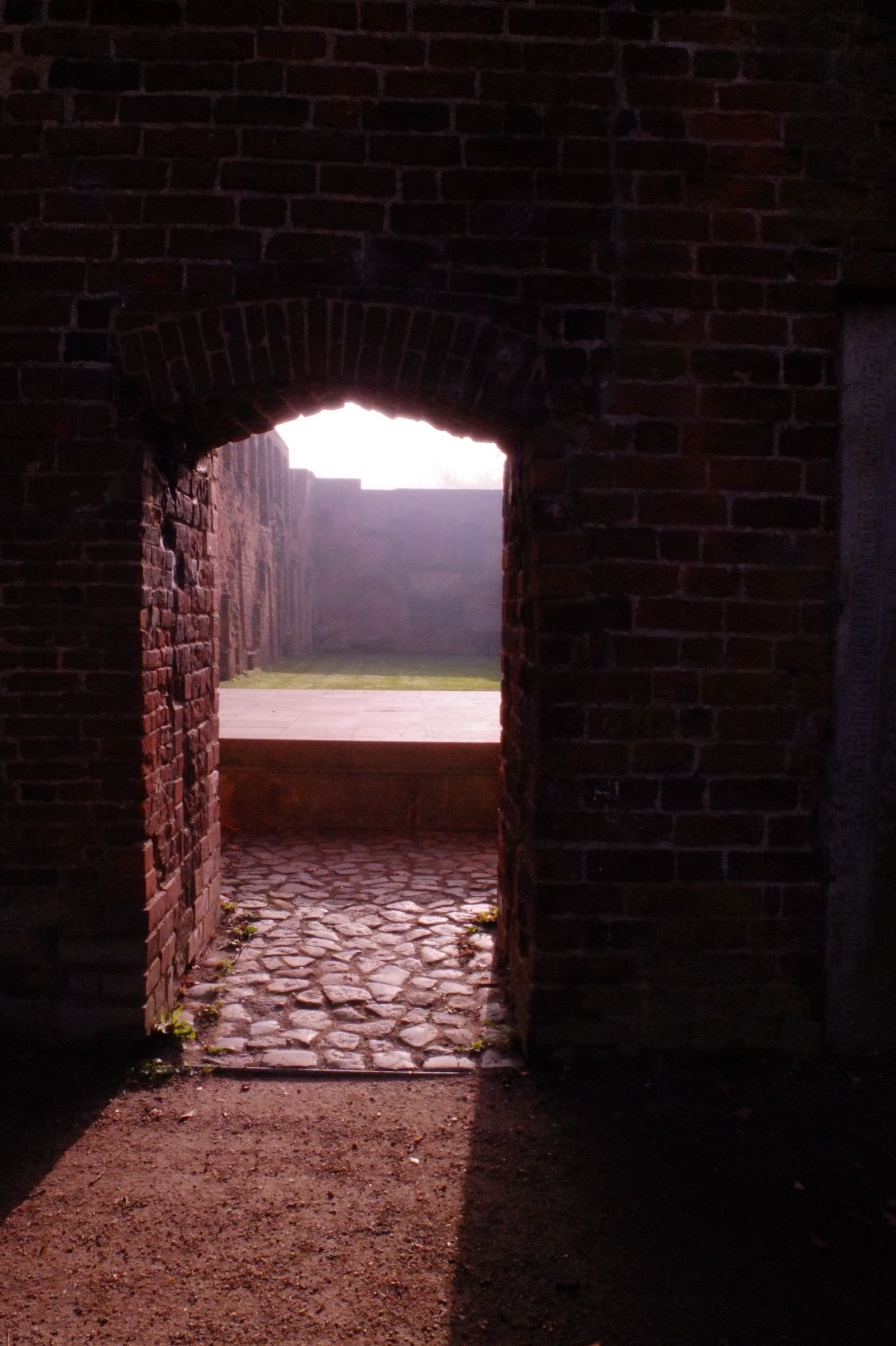 Dark brick passage opening onto a sunlit courtyard