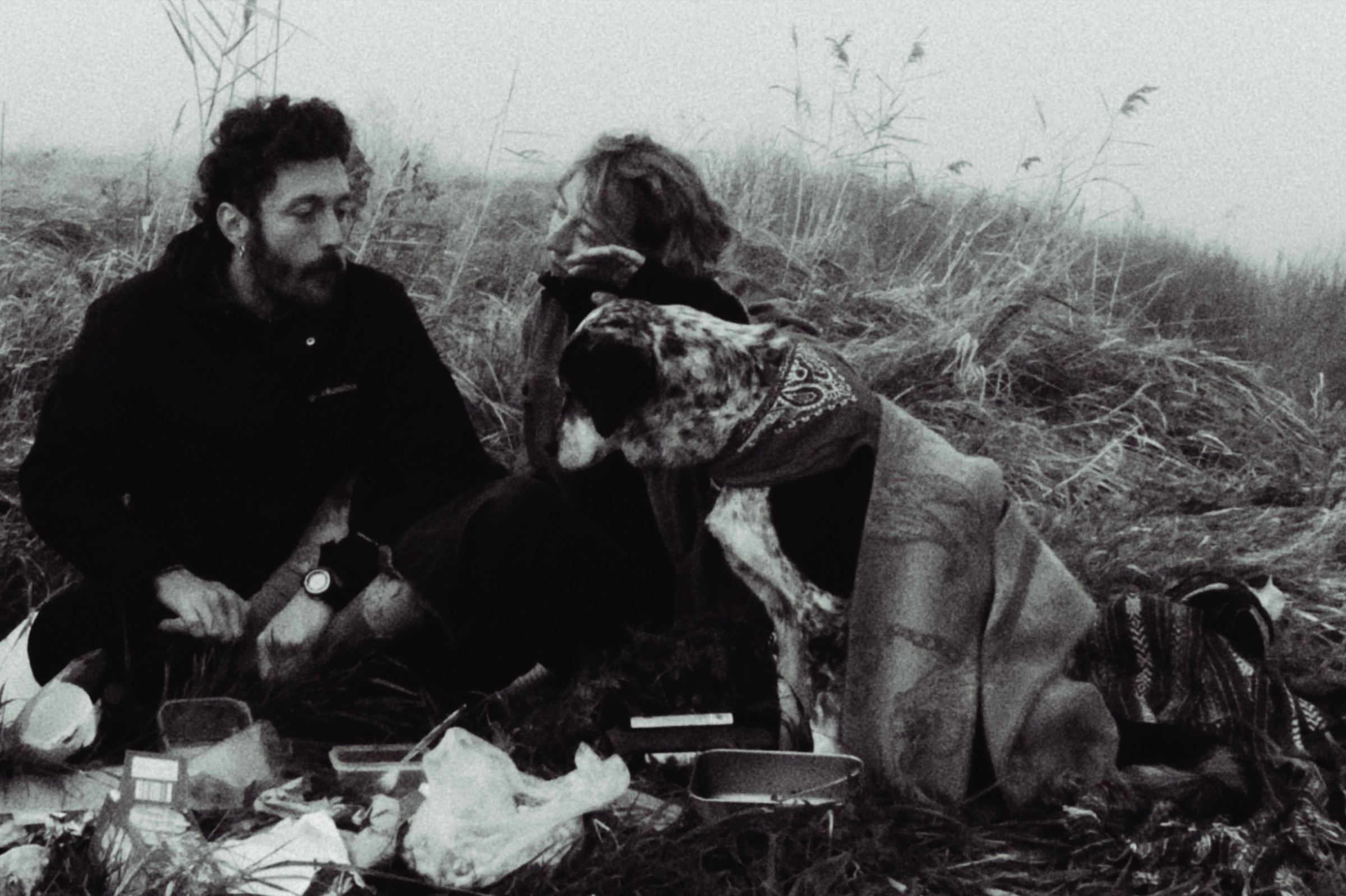 Two people and a dog sitting in a field