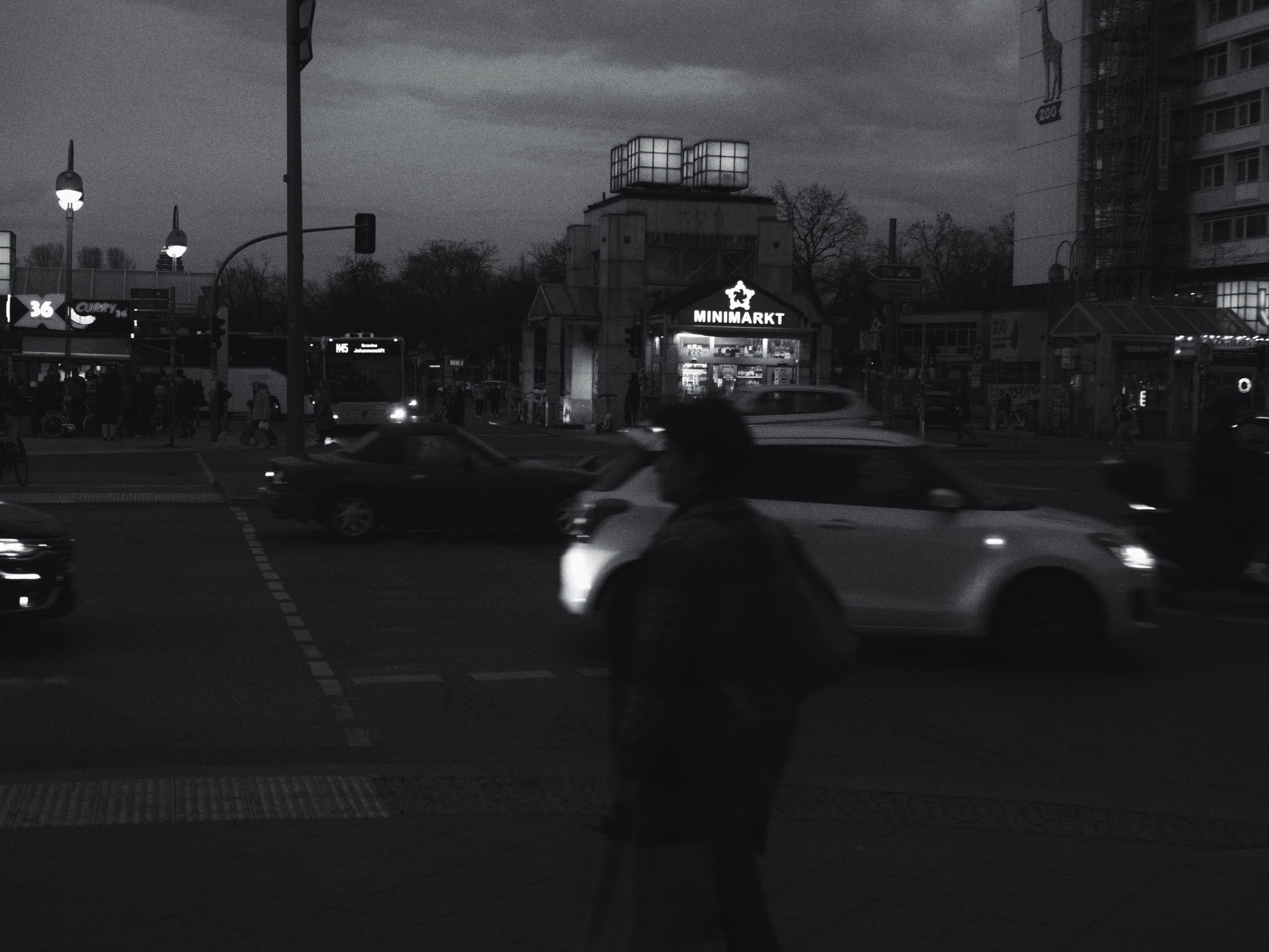 Figure crossing a street corner at night by a lit kiosk