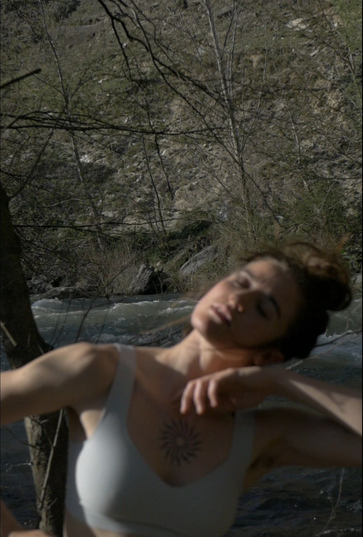 Woman with closed eyes by a river, arm over her head