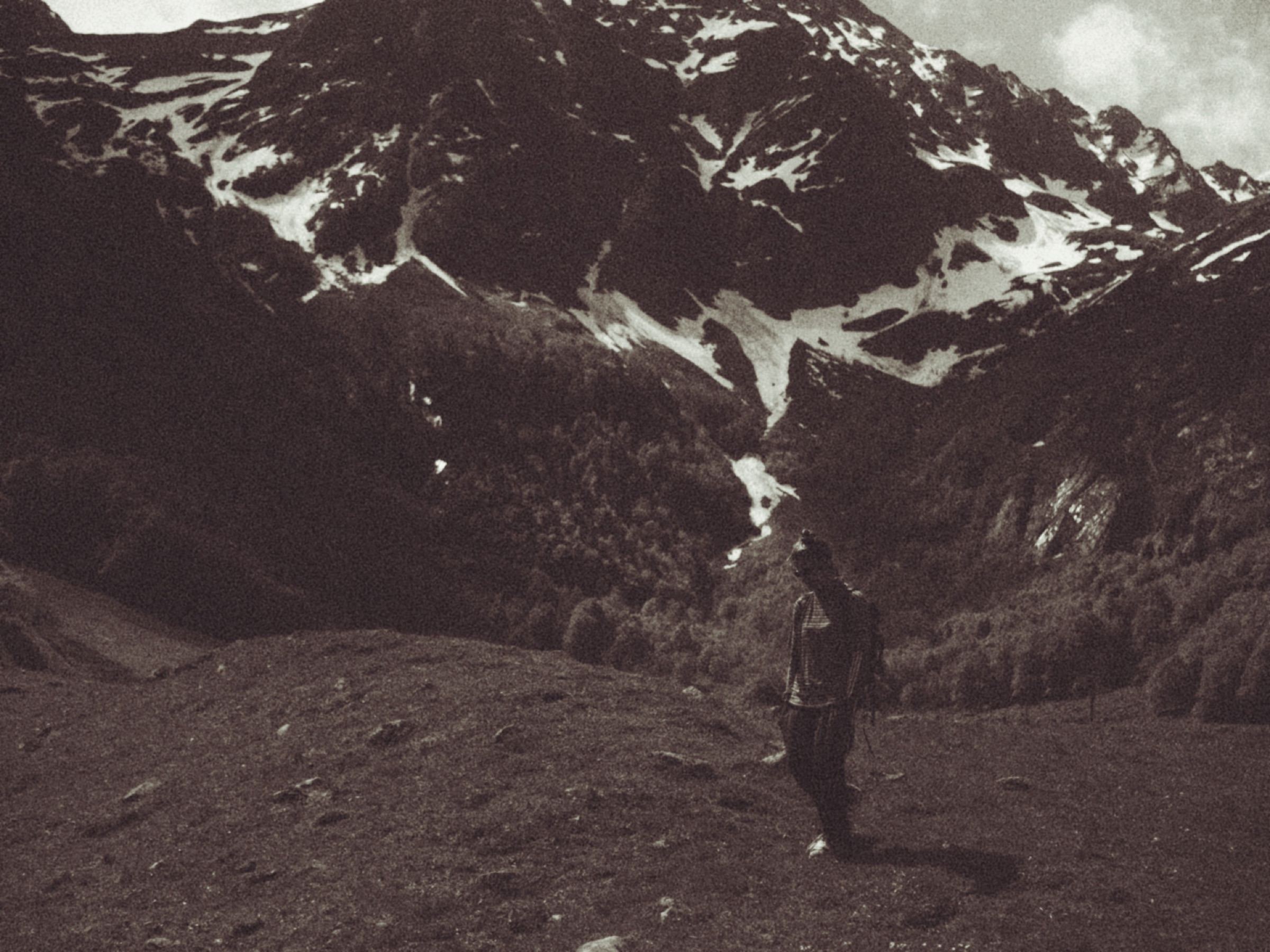 Figure walking below a snowy mountain, sepia-toned