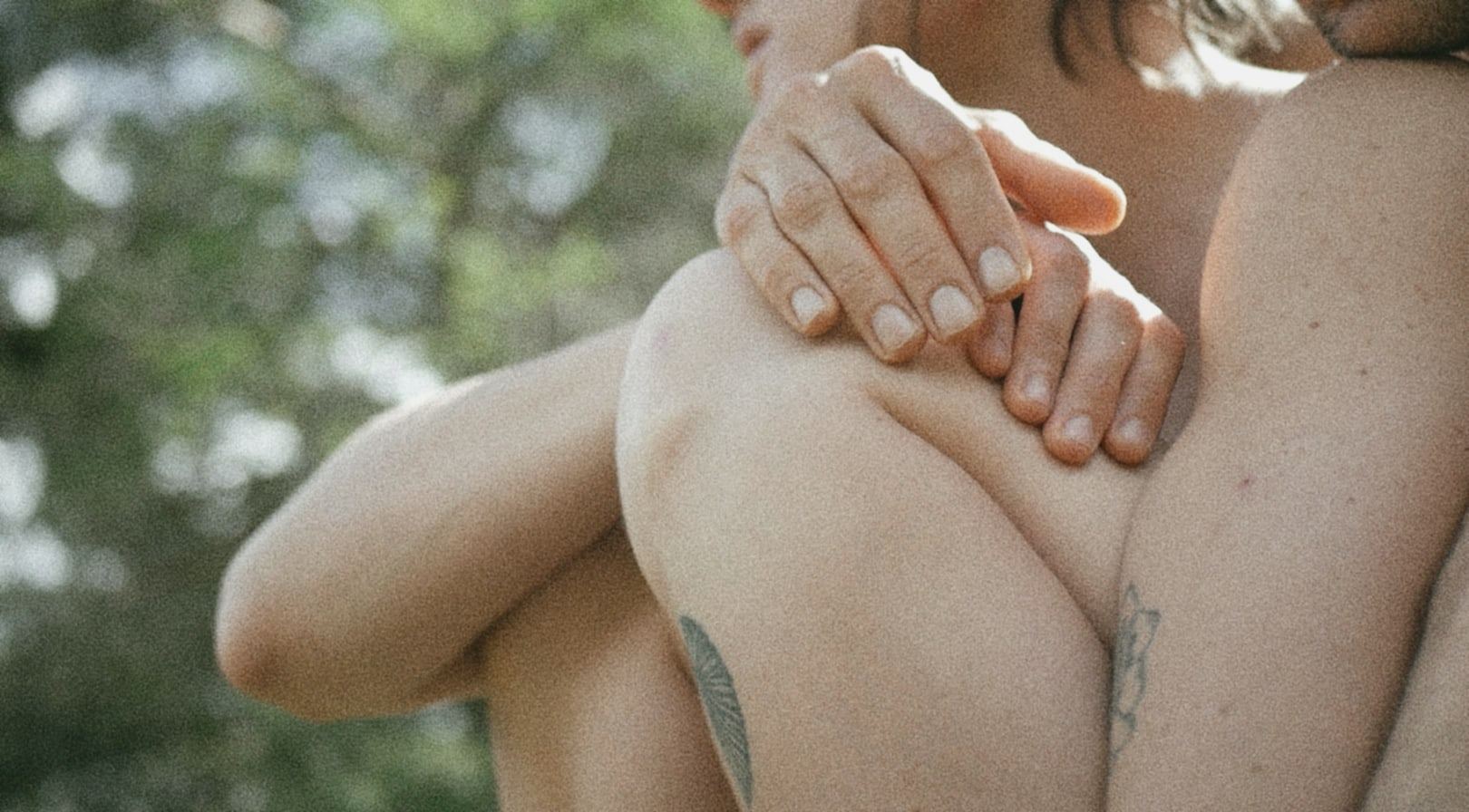 Hands embracing a bare back, trees behind
