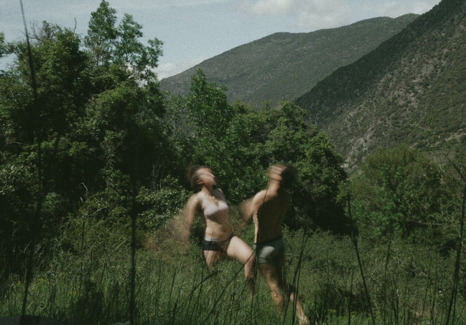 Two people running through tall grass in a green valley