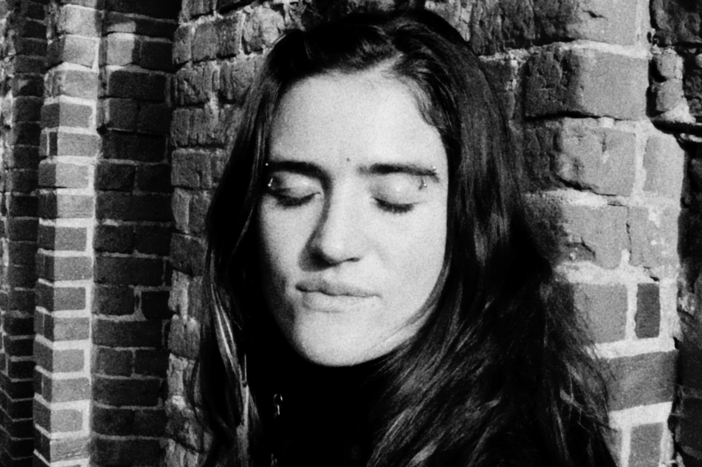 Woman with closed eyes against a brick wall