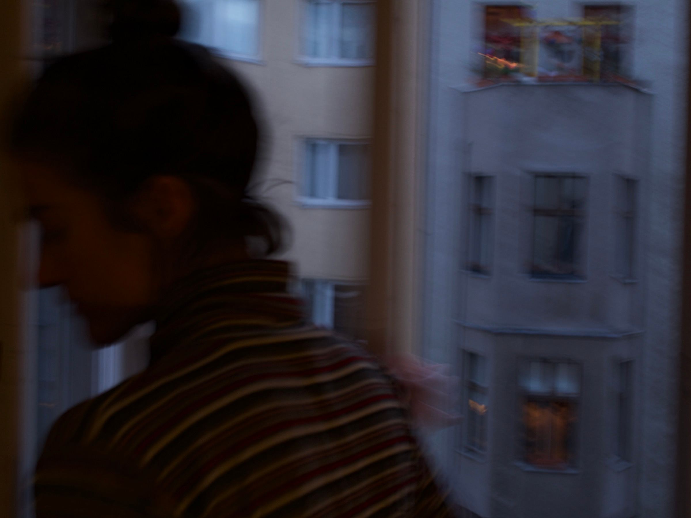 Blurred figure in a striped sweater by a window, apartment blocks outside