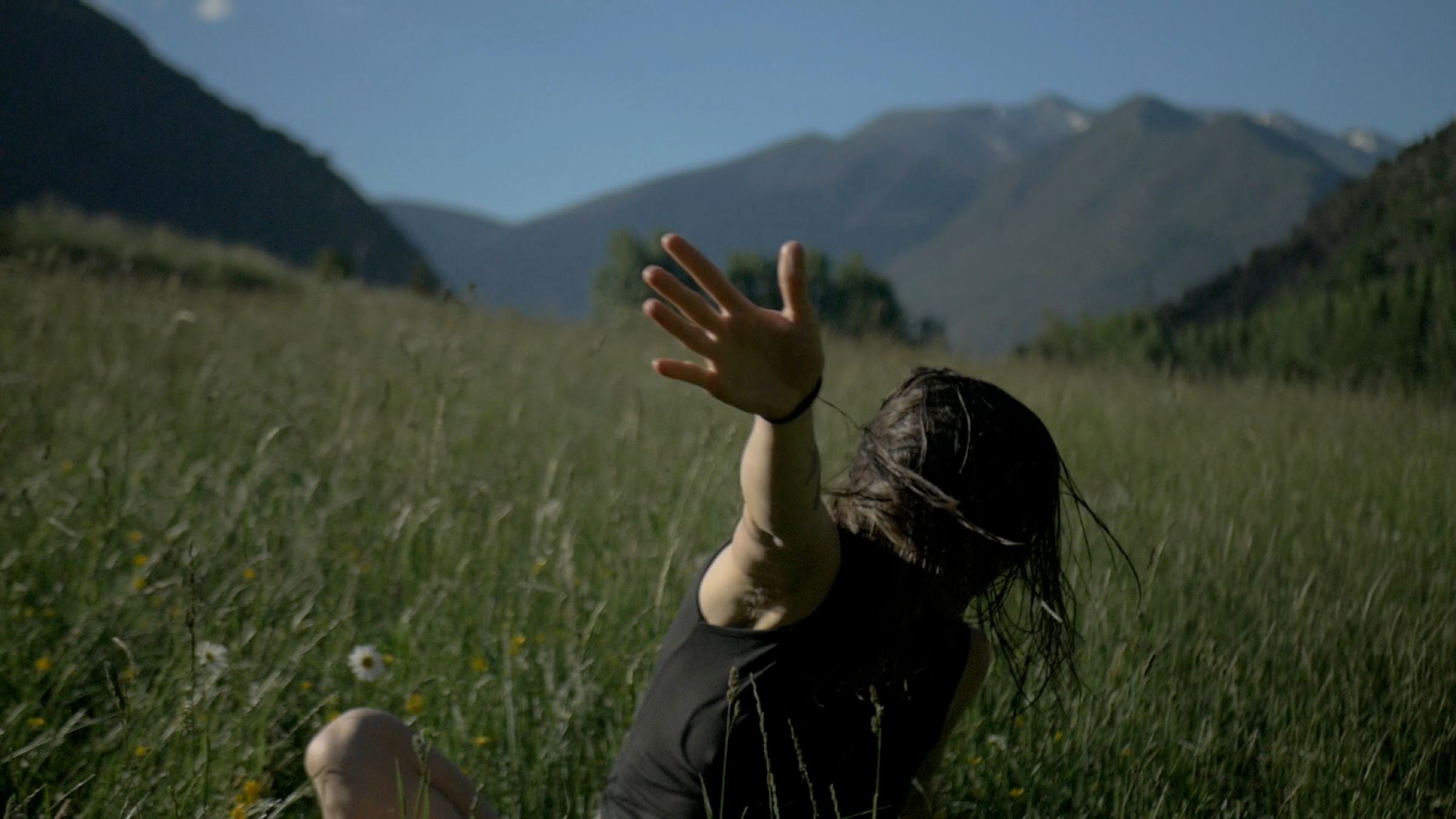 Woman raising a hand in tall grass below the mountains