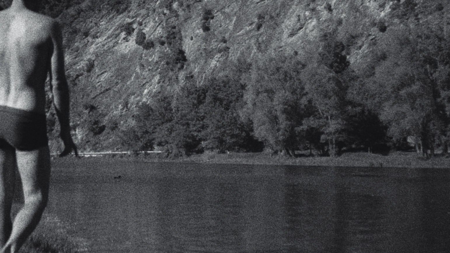 Man in swim trunks walking by a lake