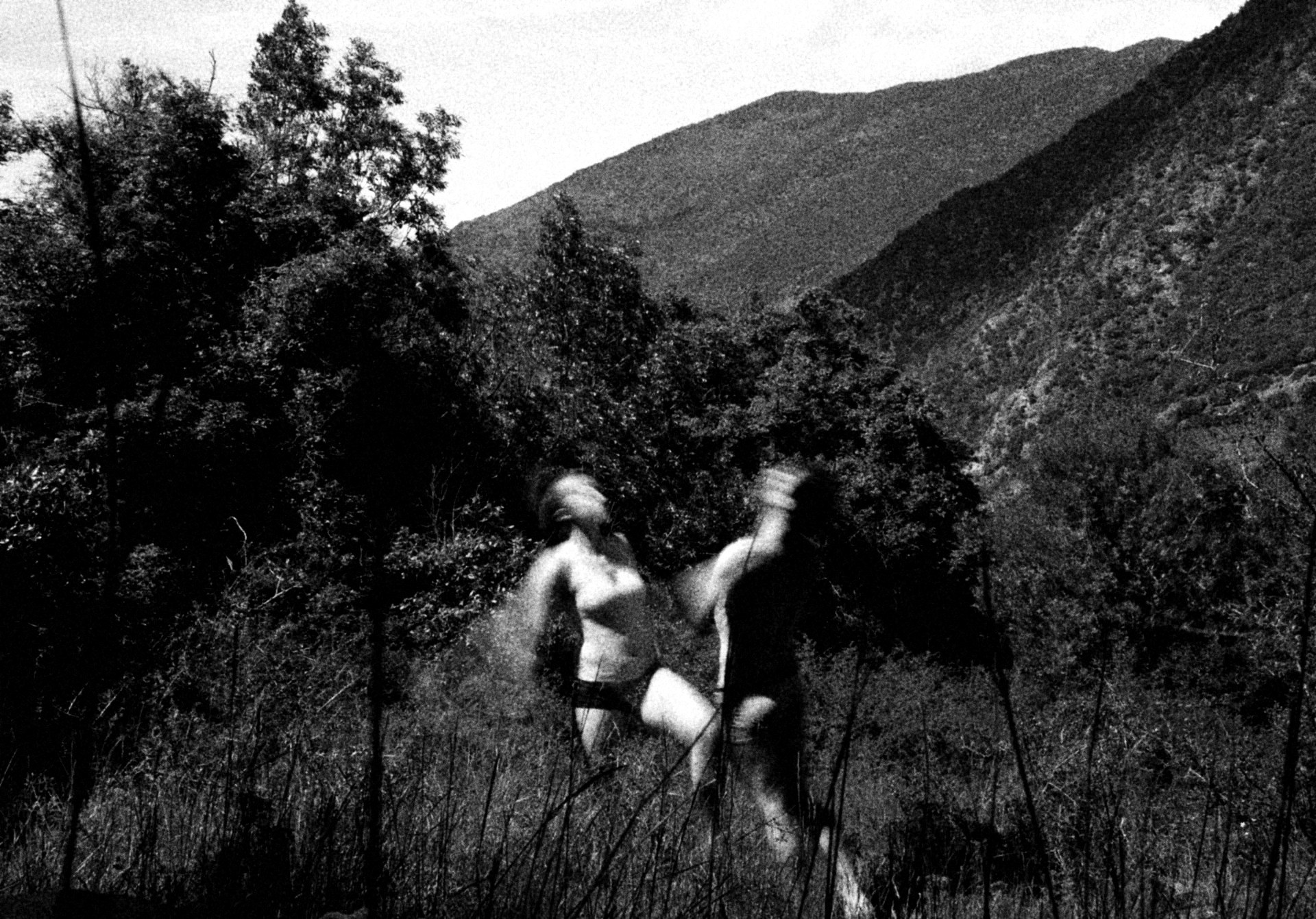 Dos personas corriendo entre pastos altos en un valle, en blanco y negro